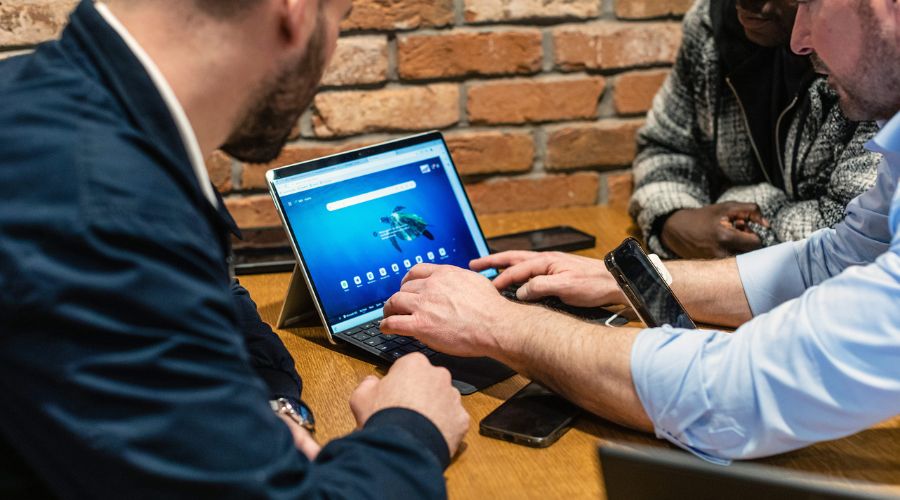 Three business team members around a laptop, preparing for the 2025 digital switchover. 