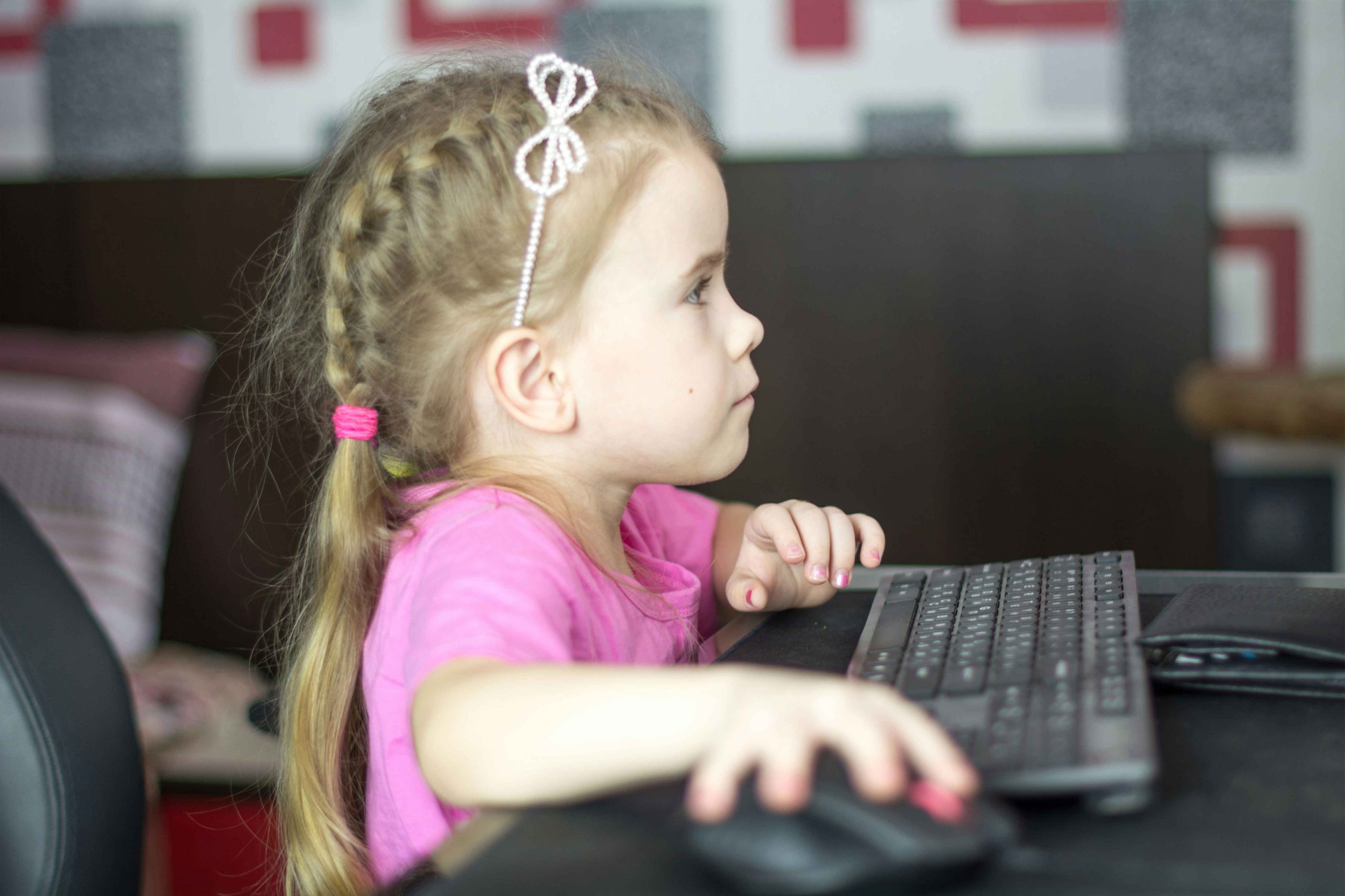 A young girl sitting at a computer. We see her in profile. Her right arm is stretching out to reach the mouse. She looks engaged in the screen.)